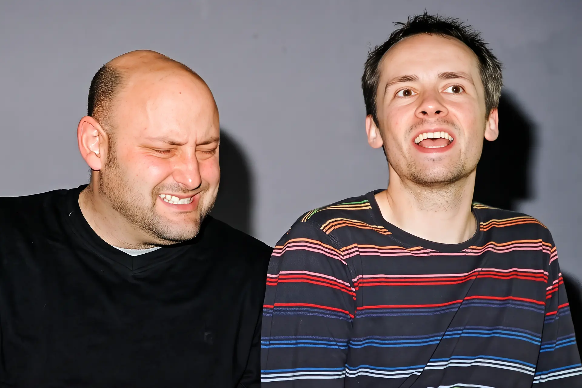 Two actors playing the ceilidh scene as a crowded bar, one with his eyes screwed shut and teeth bared, the other with his head tilted back and mouth wide open.